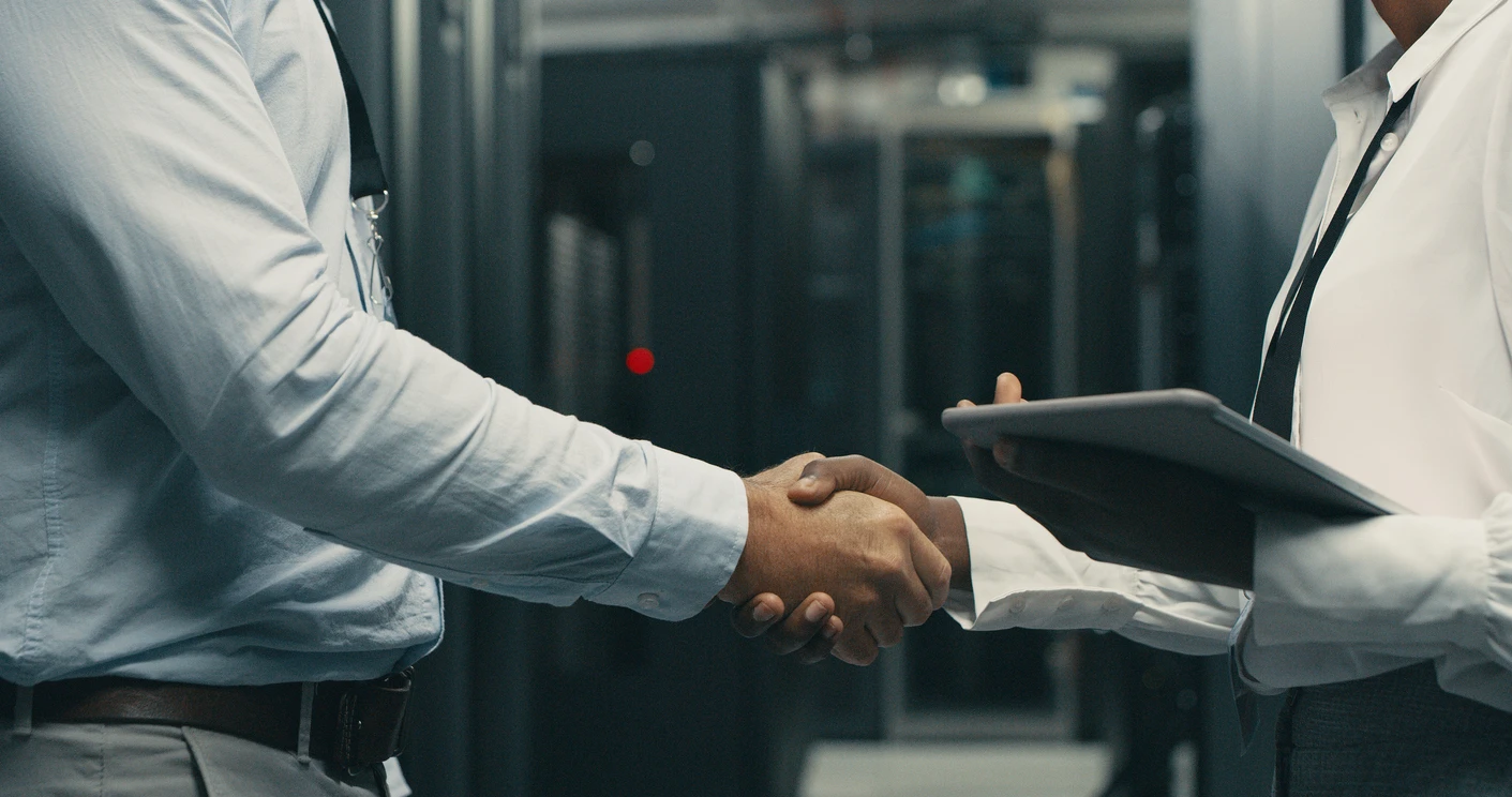 Two IT professionals shaking hands in a server room, symbolizing a potential change or upgrade in IT support services