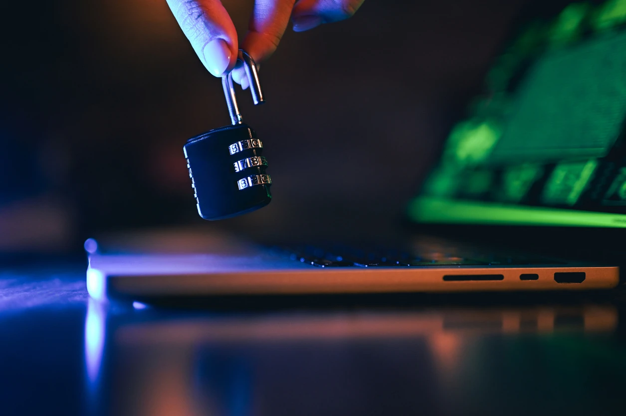 Hand holding an open combination padlock above a laptop with coding display, symbolizing Cyber Security and data protection