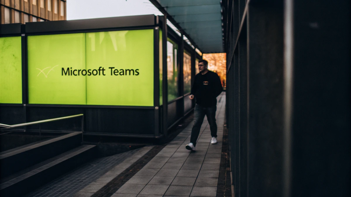 A person walking past a Microsoft Teams sign in an outdoor corridor, representing modern workplace collaboration tools